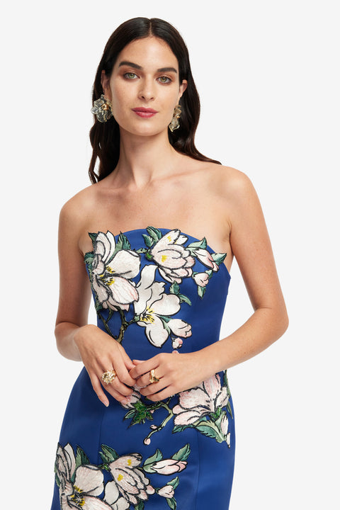 Up close of a woman wearing a blue strapless dress with floral patterns on a white background.