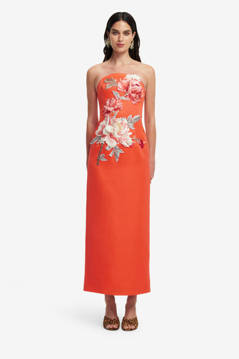 Woman wearing an orange strapless maxi dress with floral patterns on a white background.