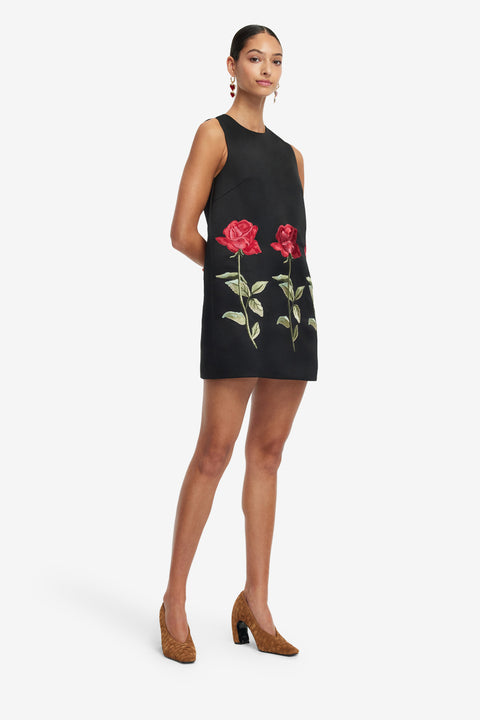 Woman posing, wearing a black mini dress with floral embroidery on a white background