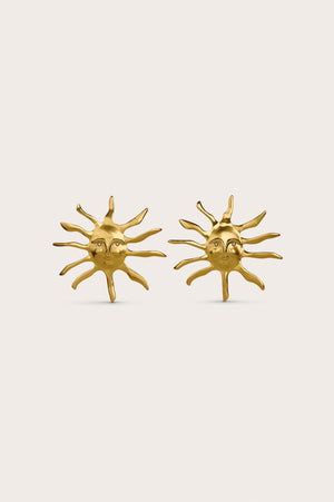A pair of gold-toned statement earrings designed like an abstract sun that features a face with glass pearl eyes.