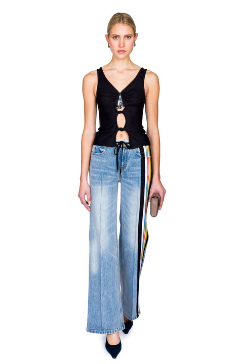 Woman wearing a black cutout top with a crystal pendant and black skirt with a brown bag on a white background with one foot in front of the other.