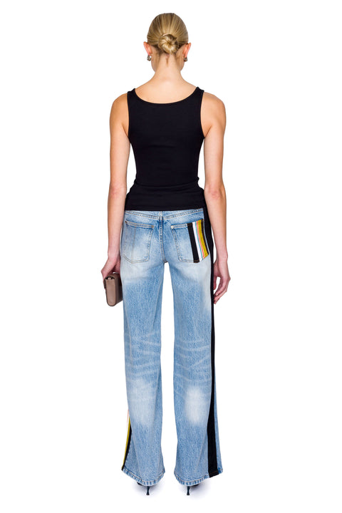Woman wearing a black cutout top with a crystal pendant and black skirt with a brown bag on a white background from the back.