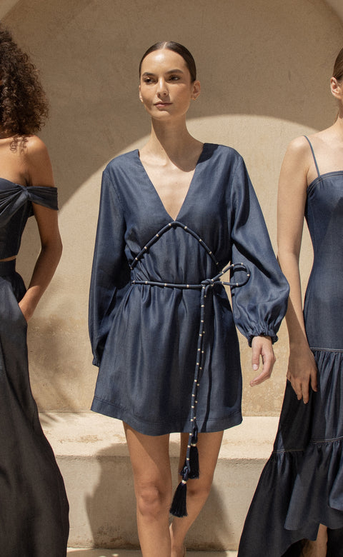Model poses in blue denim mini dress with rope belt and v-neck.