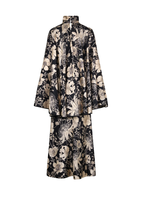A two-piece matching set featuring a long-sleeved high-neck jacket and a long skirt, both decorated with a large-scale beige and cream floral pattern on a black background.