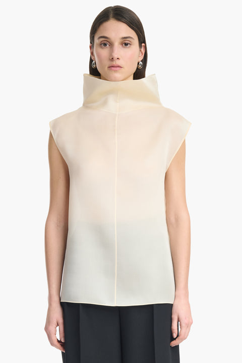 Zoomed in view of woman wearing a translucent high-neck sleeveless cream top and black pants on a white background