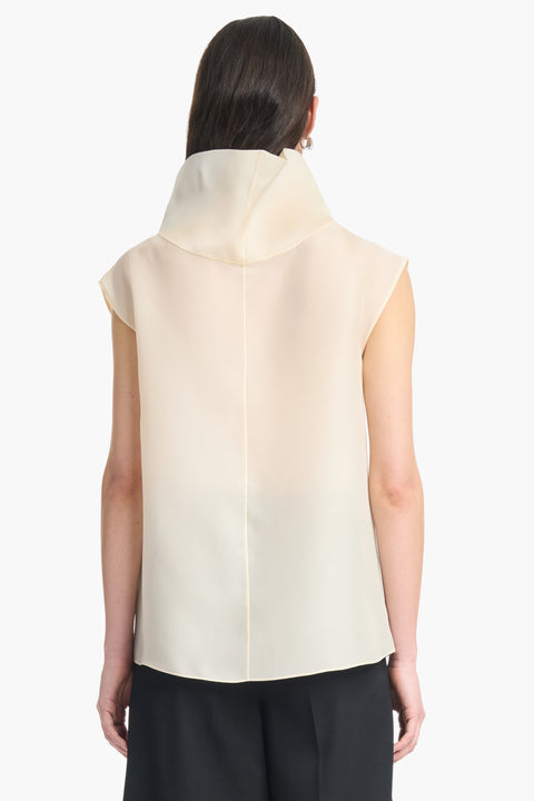 Back view of woman wearing a translucent high-neck sleeveless cream top and black pants on a white background