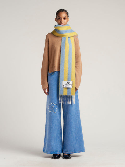 Model wears a blue and yellow striped scarf with cream tassels.