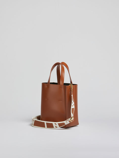 Brown leather tote bag with a strap on a light gray background