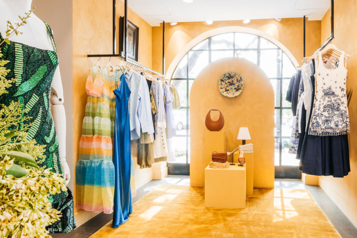 Image inside the Market x Staud pop up space with yellow lime wash walls, black clothing racks, and display pedestals.
