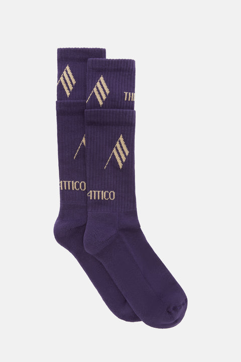 Flat lay image of a pair of purple socks with contrasting gold logos and a layered effect.