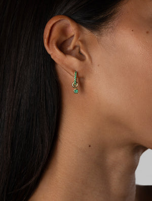 Close-up of an ear wearing a green gemstone earring with a dark background