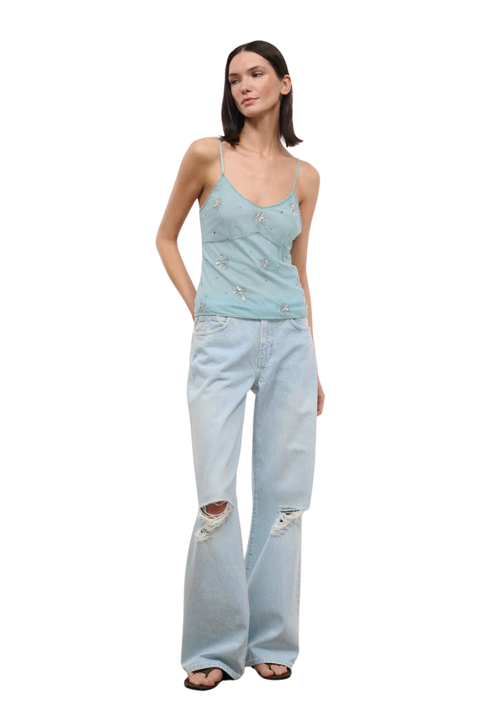 Woman wearing a light blue denim tank top with embellishments on a white background side
