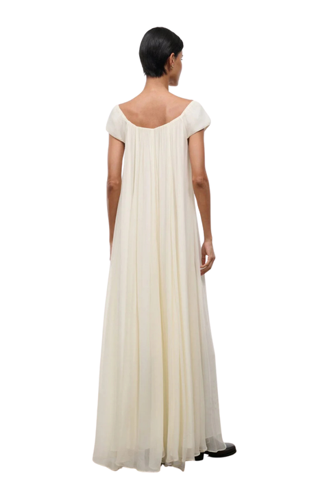 A woman wearing a long ivory dress with short cap sleeves and an elastic neckline back angle
