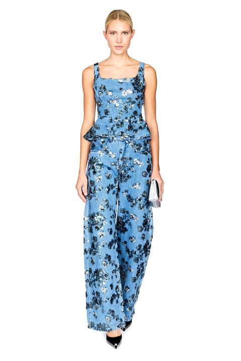 A model wearing a sleeveless denim floral top with a peplum waist with matching jeans, photographed against a solid white background.