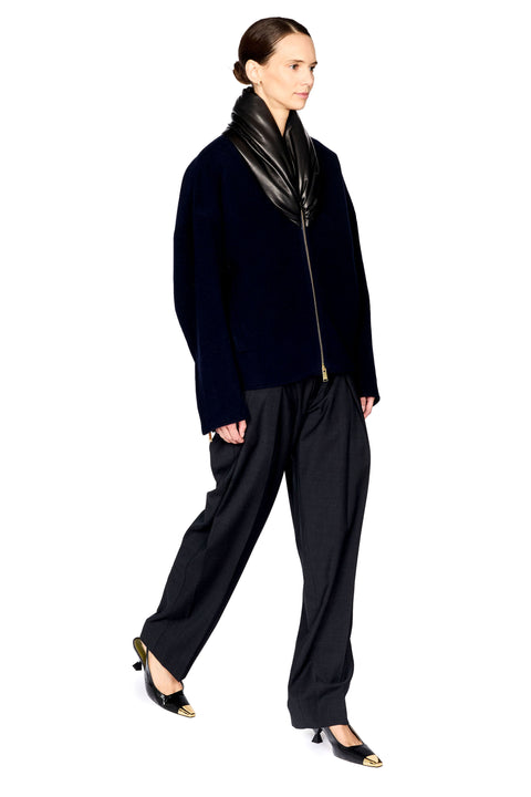 A model wearing a black velvet zip-up jacket with a glossy black collar, black wide-leg trousers, and black pointed-toe heels with gold accents, set against a plain white background.