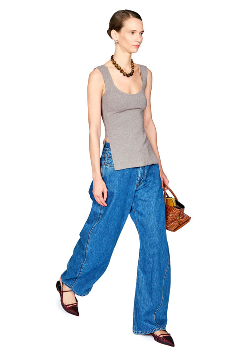 A woman modeling a gray ribbed tank top, wide-leg blue jeans, dark brown pointed flats, a brown beaded necklace, and holding a small brown woven handbag against a plain white background.
