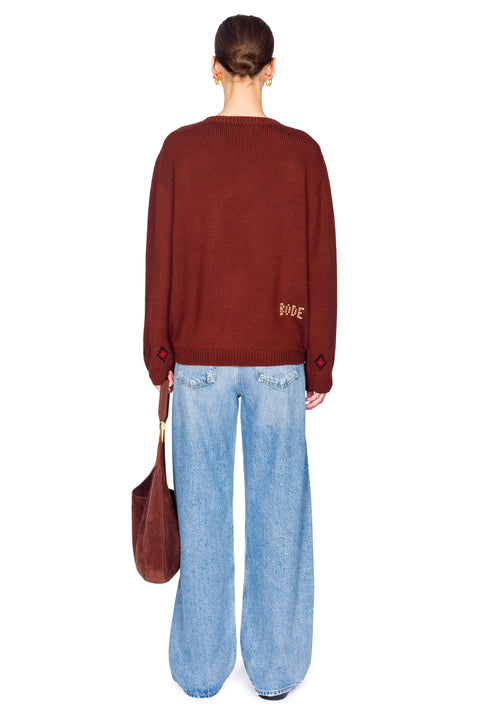 Person wearing a brown sweater with dog designs, blue jeans, and carrying a brown bag on a white background from the back.