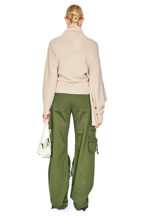 A model shown from the back wearing a beige knit wrap sweater and olive green wide-leg cargo pants, holding a white handbag against a plain white background.