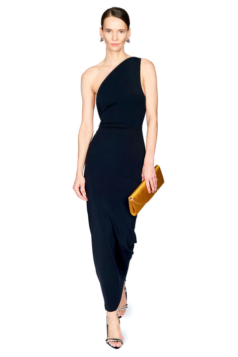 A woman modeling a black one-shoulder maxi dress with draped side details, holding a metallic gold clutch against a plain white background.