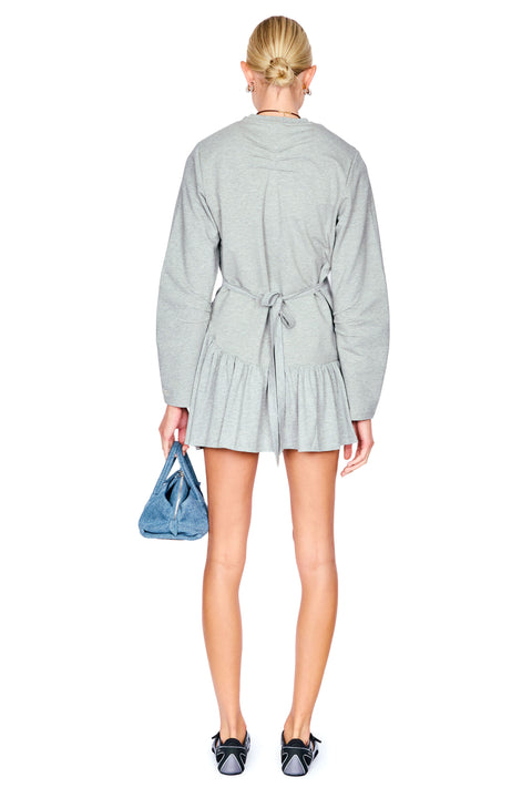A model shown from the back wearing a light gray long-sleeve wrap mini dress with a tie waist, holding a blue handbag against a plain white background.