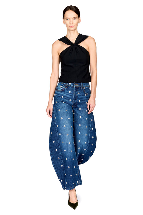 A model wearing a black halter-neck top and blue wide-leg jeans with white floral embroidery, standing against a solid white background.