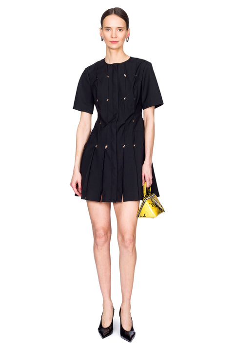 Woman wearing a short black origami dress with a yellow snakeskin bag with one foot in front.