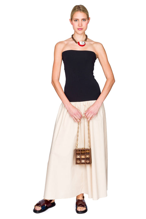 Woman wearing a black and beige dress with a handbag on a white background clutching her bag.