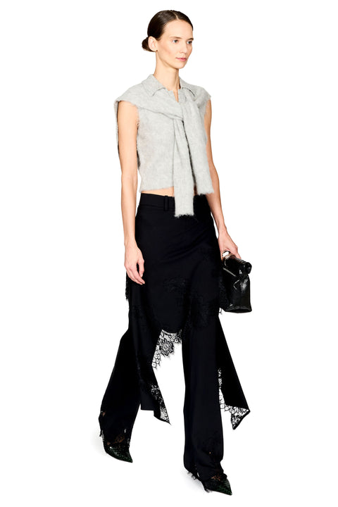 A model wearing a light gray sleeveless knit top with a draped collar, black wide-leg trousers with lace trim, and holding a small black handbag against a plain white background.