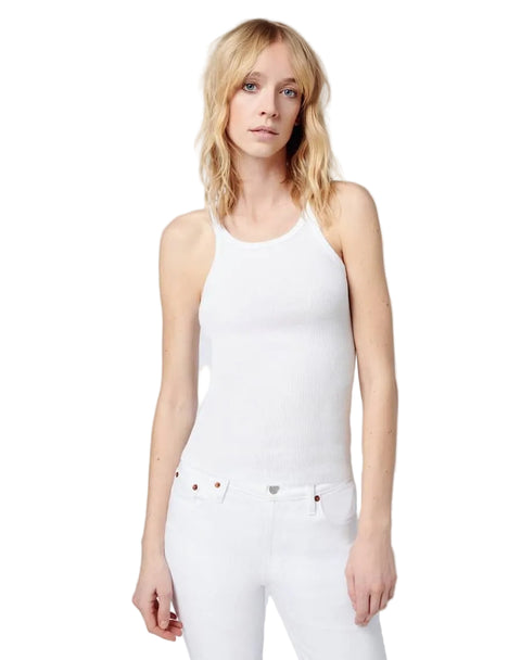 Woman wearing a white tank top and white pants against a plain background