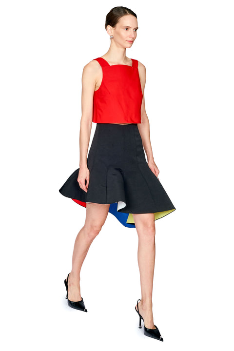 A model wearing a sleeveless red crop top and a black flared skirt with a colorful geometric pattern on the hem, paired with black pointed-toe heels, against a plain white background.