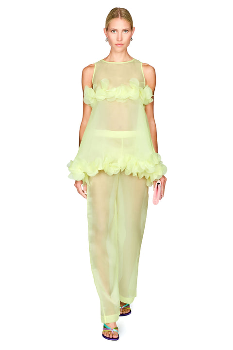 A model wearing a sheer pale yellow-green two-piece outfit with a ruffled halter-style top and matching wide-leg pants, photographed against a plain white studio background.