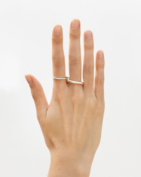 A woman's hand wearing a Spinelli Kilcollin Agon ring that features a 1.7mm sterling silver band and a 3.8mm sterling silver textured band connected by two yellow gold connectors across two fingers