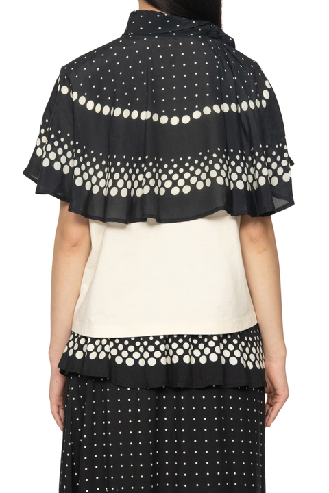 A model shown from the back wearing a black and white polka dot draped cape-style shawl over a cream top and black polka dot skirt.