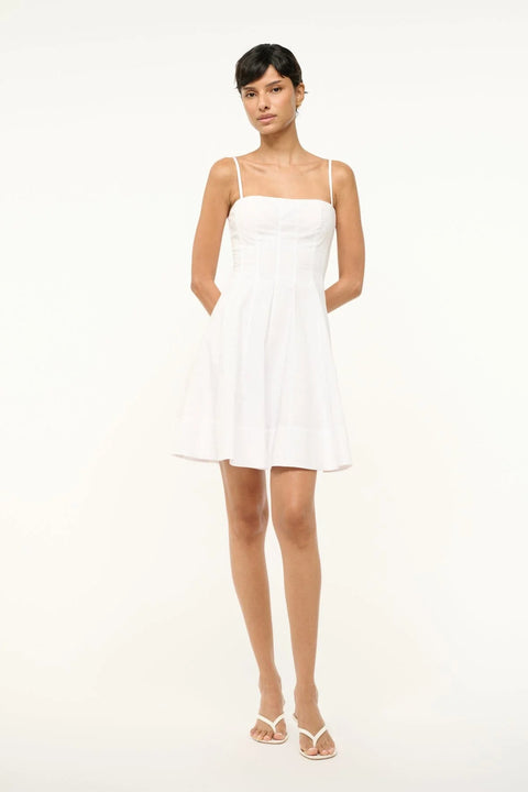 Woman wearing a white poplin mini dress that features a square neck with spaghetti straps, a fitted bodice with corset-style paneling, and a full skirt. 