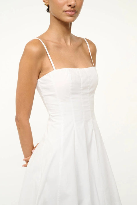 Close up of a woman wearing a white poplin mini dress that features a square neck with spaghetti straps, a fitted bodice with corset-style paneling, and a full skirt. 