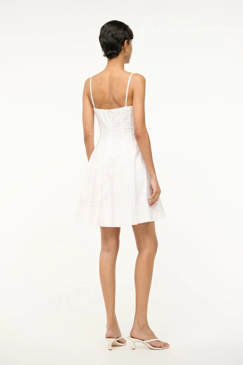 Back view of a woman wearing a white poplin mini dress that features spaghetti straps, a fitted bodice with corset-style paneling, and a full skirt. 