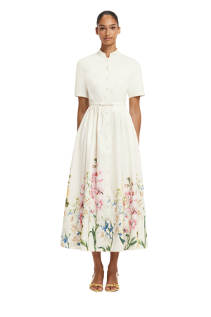 A woman modeling a white midi dress with short sleeves, a button-front bodice, and a colorful floral print concentrated along the lower skirt, photographed against a plain white background.