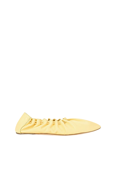 A pale yellow leather slip-on shoe with a gathered, ruched upper and a pointed toe, shown in profile against a solid white background.