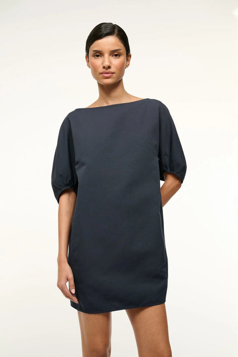 Close up of a woman wearing a navy, mini shift dress that features a boat neck and balloon half-sleeves.
