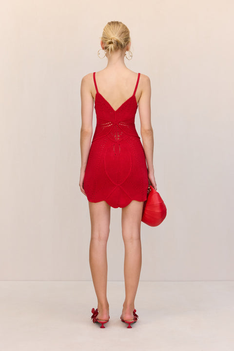 Back view of a woman wearing a red crochet mini dress that features a floral design and keyhole cutouts at the bust, paired with red accessories. 