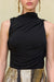 Detail shot of a woman wearing a black sleeveless top that features an asymmetrical high neck and ruched draping, paired with an embellished skirt. 