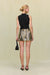 Back view of a woman wearing a sleeveless black top that features an asymmetrical high neck and draping throughout the body, paired with an embellished mini skirt and black accessories. 
