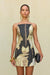 Close up of a woman wearing a strapless mini dress featuring a sculptural neckline and a black and tan portrait print depicting two women's faces looking at each other and holding a fruit in the hands. 
