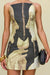 Detail shot of a woman wearing a strapless mini dress that features a sculptural neckline and a black and tan portrait print depicting two women's faces looking at each other and holding a piece of fruit in their hands, paired with a chunky gold bangle and a black clutch. 