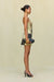 Side view of a woman wearing a strapless mini dress that features a sculptural neckline and a tan and black portrait print, paired with chunky gold jewelry a black clutch, and black heels. 