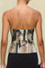 Detail shot of the back of a strapless bustier top that features a black and tan portrait print depicting two women facing each other and holding an apple. 