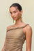 Close up of a woman wearing a gold metallic gown that features a hand rolled, one-shoulder neckline and ruched draping in the bodice, paired with gold statement earrings. 