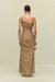 Back view of woman wearing a gold metallic gown that features a hand rolled, one-shoulder neckline and intricate ruched draping throughout the body, paired with gold heels and accessories. 