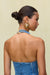 Up close back view of a woman wearing a blue denim mini dress that has a halter neck with an adjustable gold buckle detail at the back of the neck.