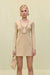 Close up of a woman wearing a cream knit, long sleeve mini dress that features a plunging wood-beaded detail and a keyhole cutout at the bust. 